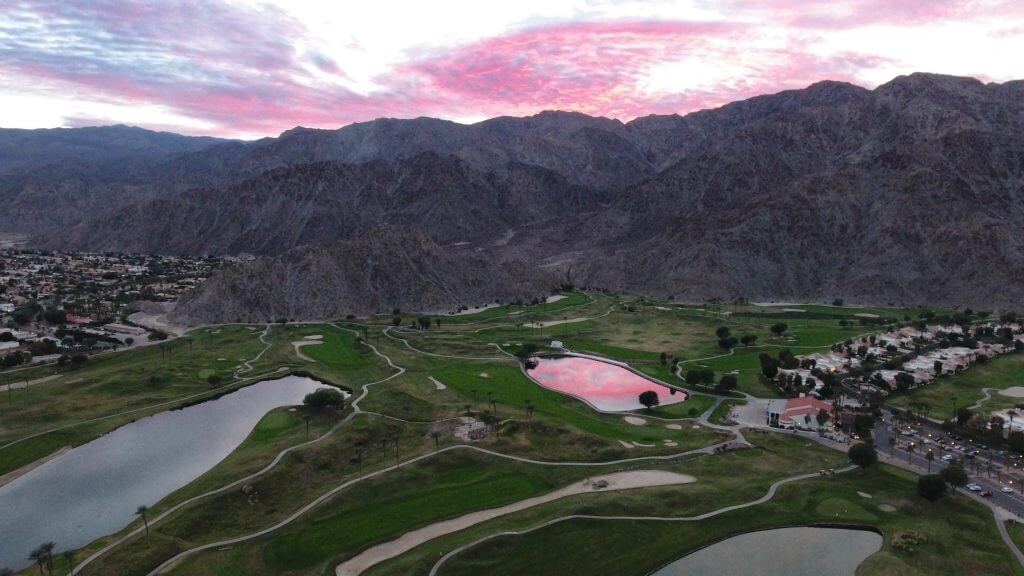 Aerial shot of a golf course with towering mountains in the background, during sunset. Palm Springs, CA is  the perfect romantic California getaway for Valentine's Day. 