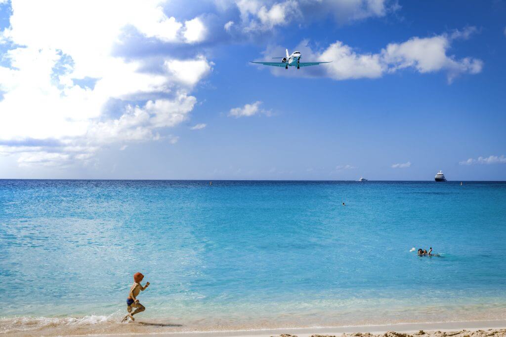 Boy runs on Maho Beach in St Maarten as a plane is coming in for a landing. 