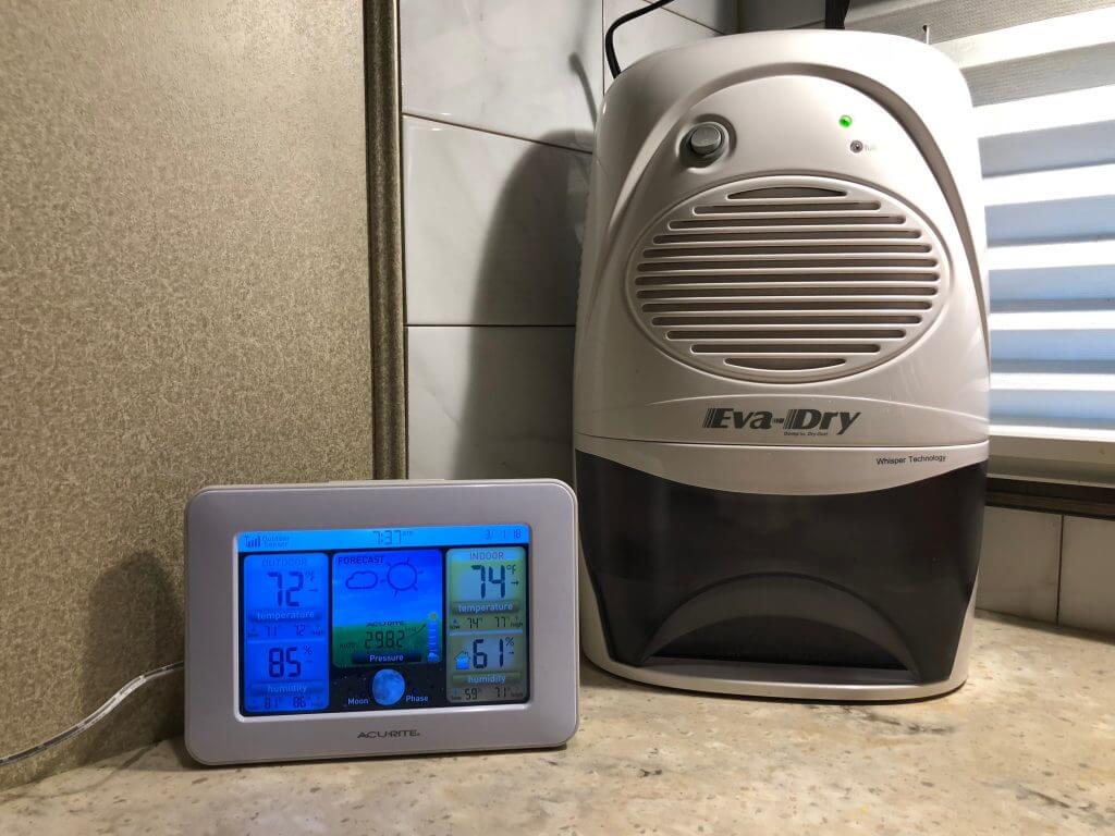 The Eva-Dry RV dehumidifier sitting on a counter with a weather station showing the humidity level is 61% inside and 85% outside 