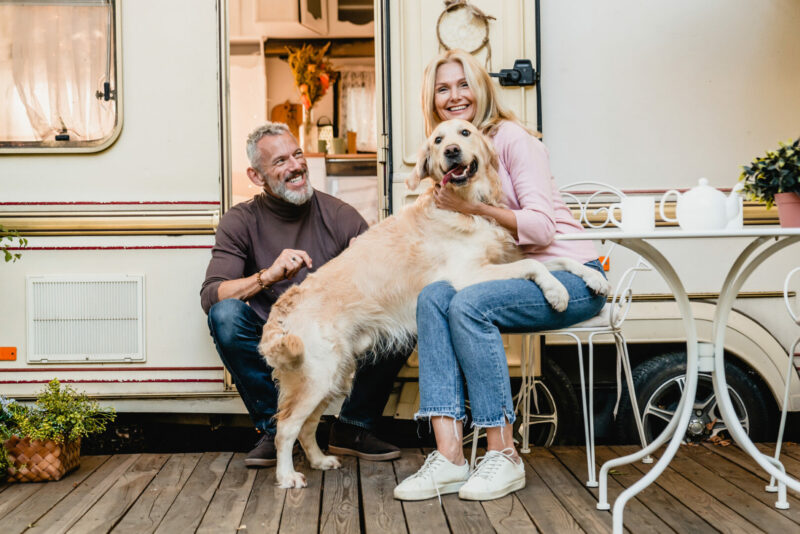 Family photo of mature couple playing with their retriever in the caravan doorway