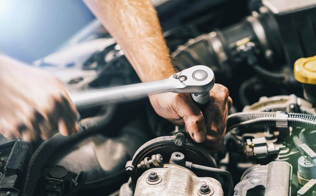 Man's hands turning wrench on engine of RV at a dealership's service department