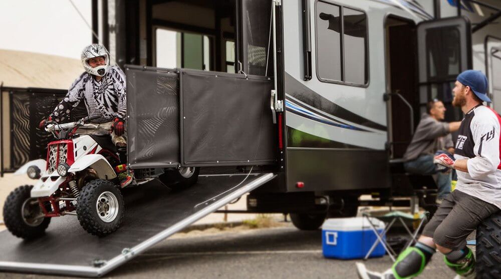 A person on an ATV driving it down the ramp of a toy hauler RV. You'll want to consider toy hauler RV floor plans if you have big toys you want to bring. 