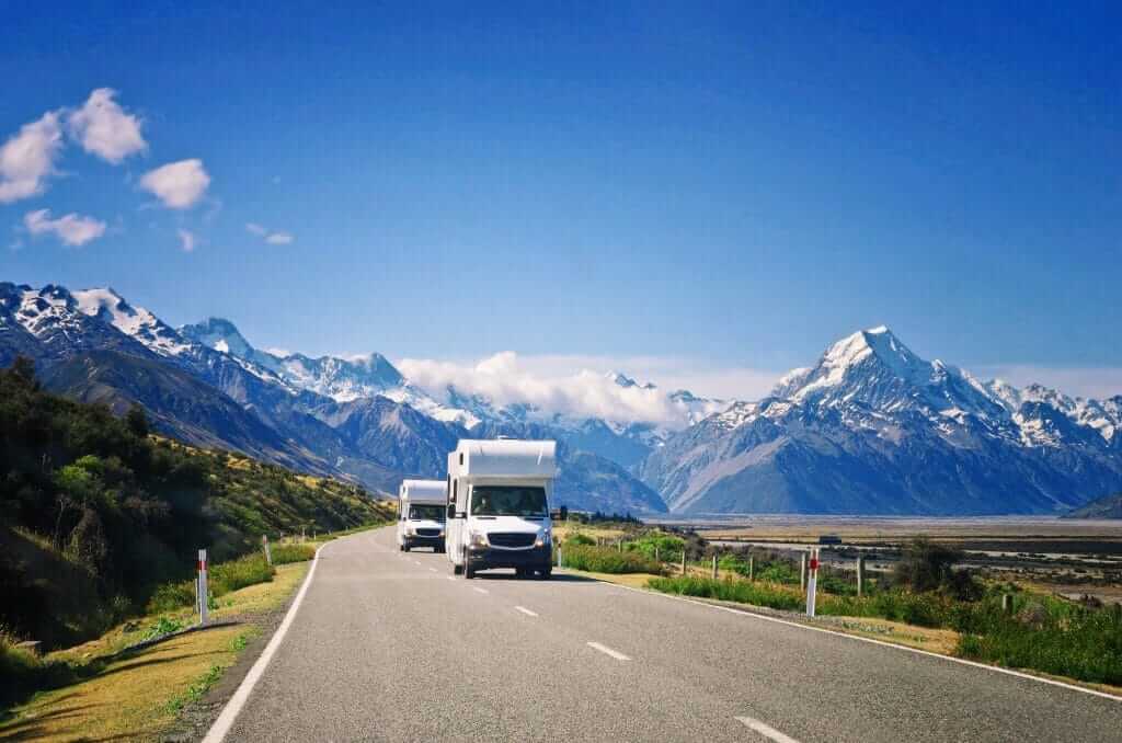 Two campers driving down the road with beautiful mountains in the background