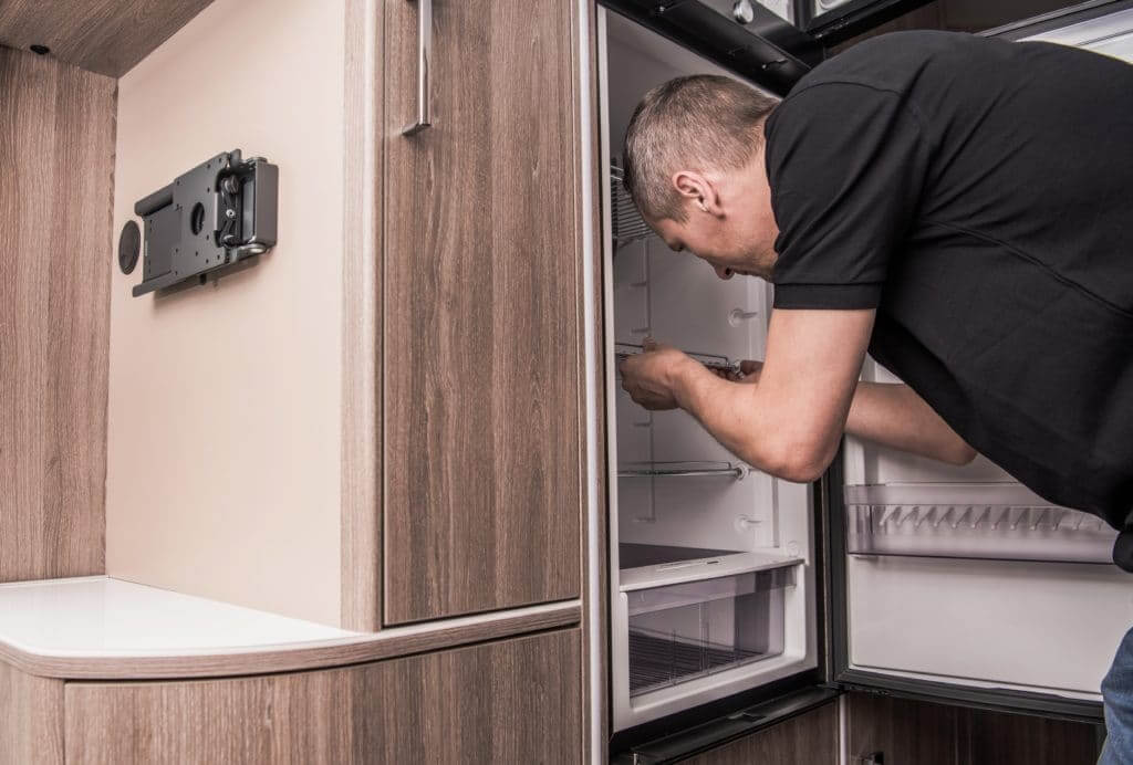 Man bending over an open fridge, conducting some RV refrigerator repair