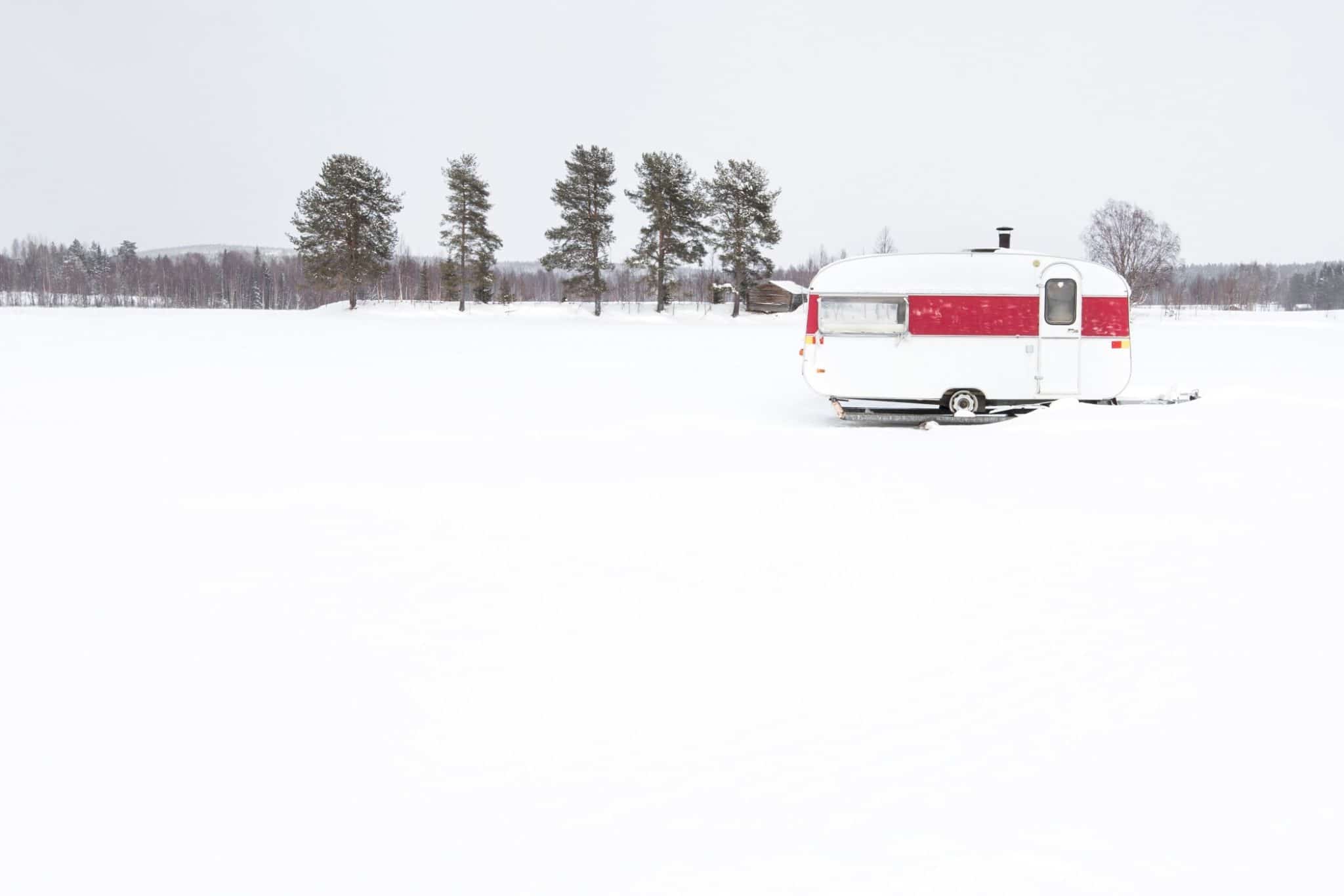 Small camper with bathrooms in the snow with trees in the background. 