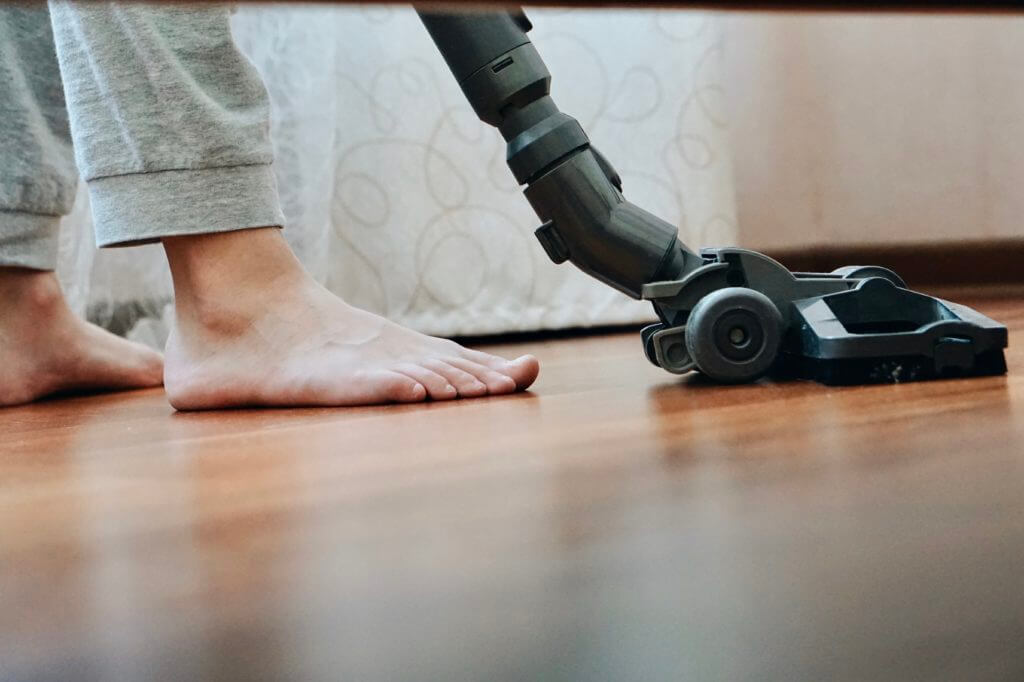 A barefoot person is using a stick vacuum to clean the vinyl floors of the RV after choosing the best corded vacuum for the RV