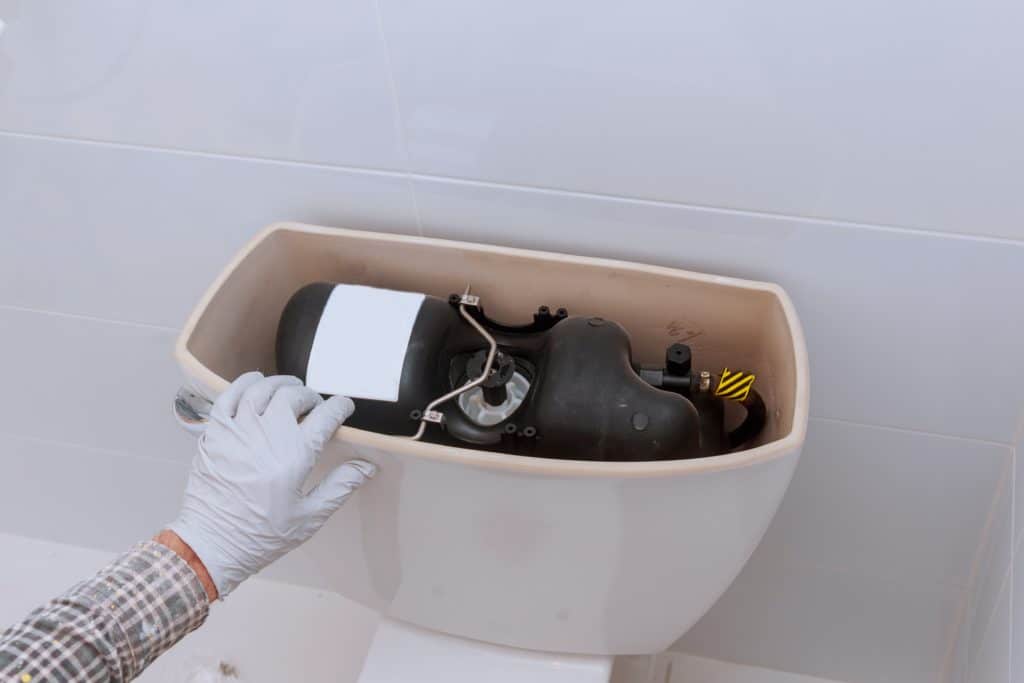 Man with gloves on opening a traditional house toilet water tank. To do RV toilet repair, you have to learn a new system. 