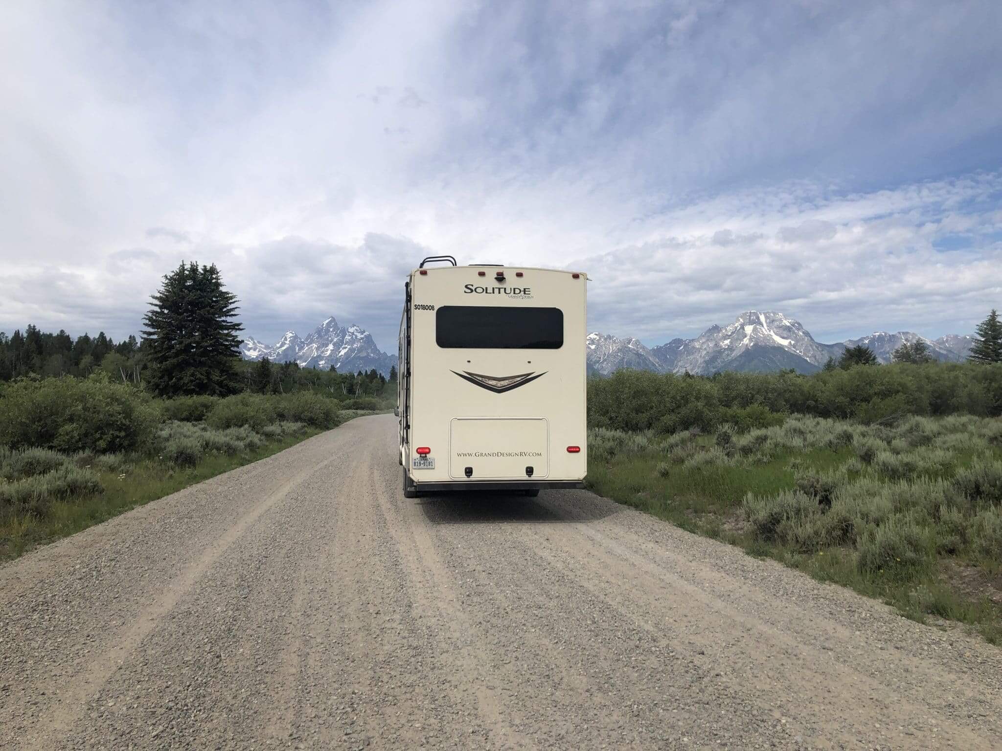Fifth wheel RV driving down a dirt road with the Grand Teton mountains in the background