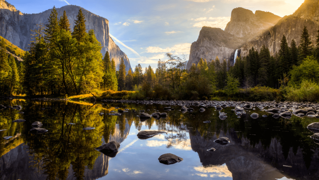 Yosemite National Park landscape is shown with mountains, trees, water, and blue skies.