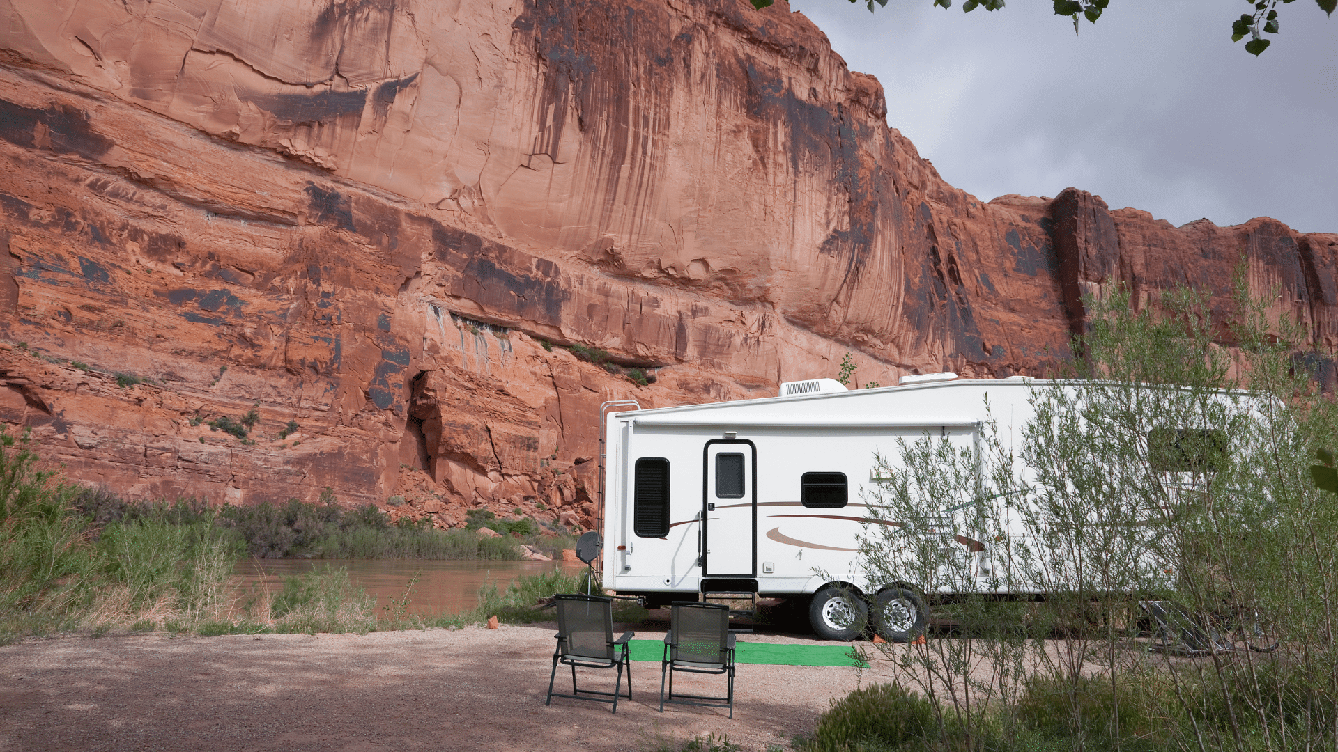 RV dry camping along a river set against a desert red rock wall.