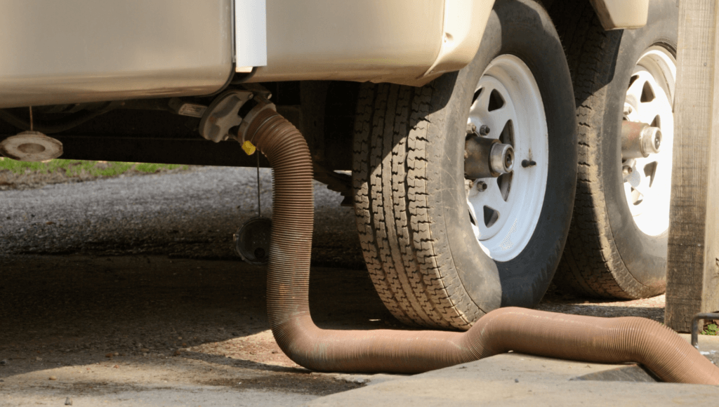 An RV sewer hose is connected to the blank tank under the RV ready to dump the black tank then rinse the tank with the best rv tank rinser.