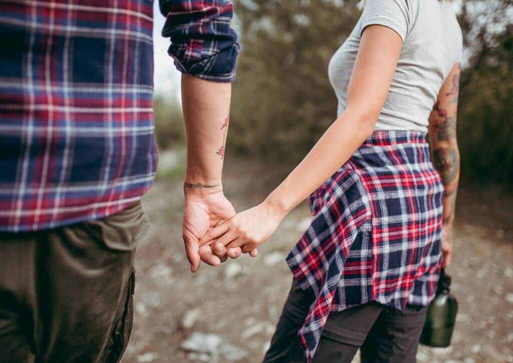 Camping couple holding hands while walking outdoors, thinking about Valentine camping ideas for each other. 