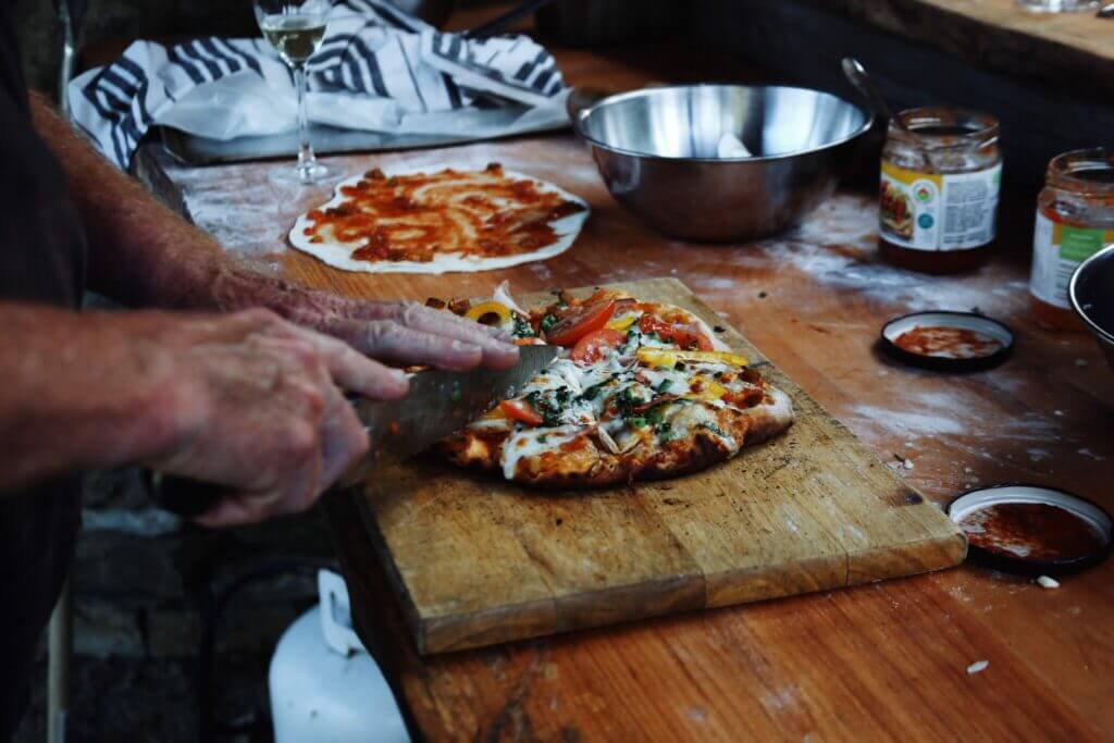 Man cutting small pizza that has been cooked in a pizza oven. A great addition to your perfect RV outside setup. 