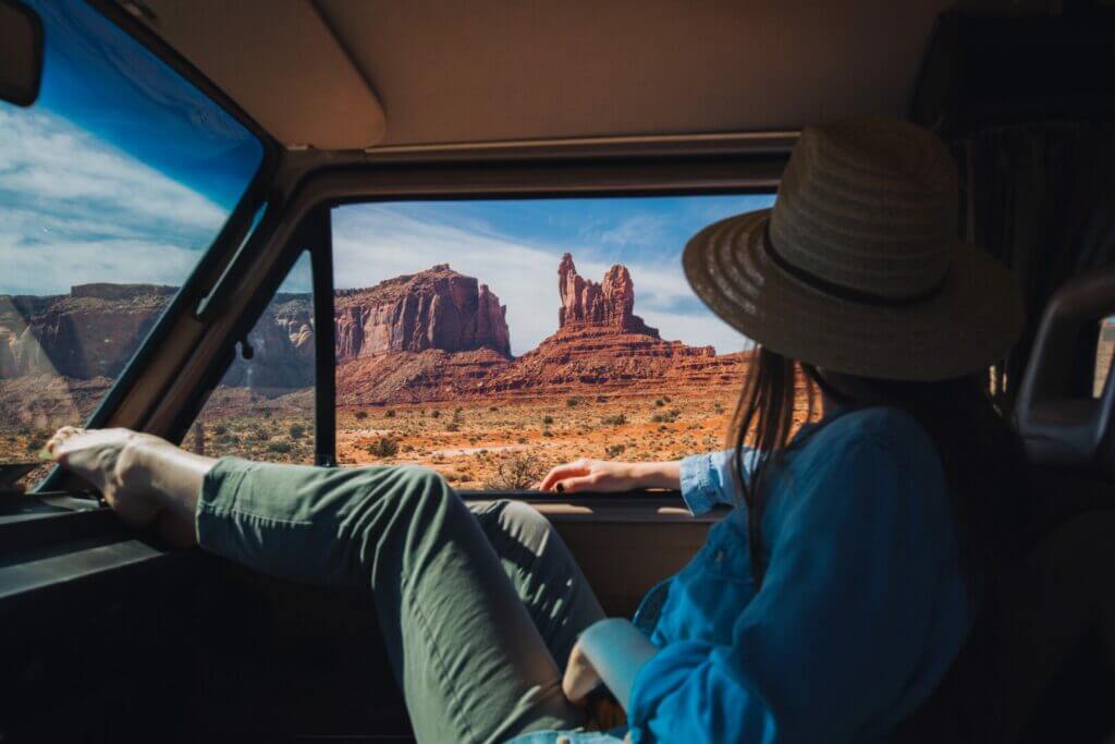 Woman sitting in the passenger seat of a van with her feet on the dash looking out her window at Monument Valley in Arizona. She learned how to plan a road trip and seeing sites like this.