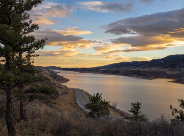 The sun sets over Horsetooth Reservoir and there are trees and a road in the foreground leading to great camping.