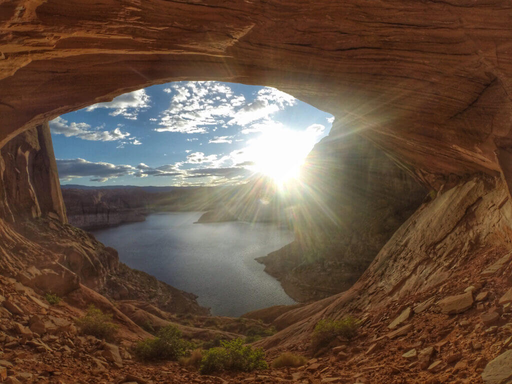 Looking through an arch at the sun setting over the lake. This is called "window to heaven" and you can see it when Lake Powell RV camping. 
