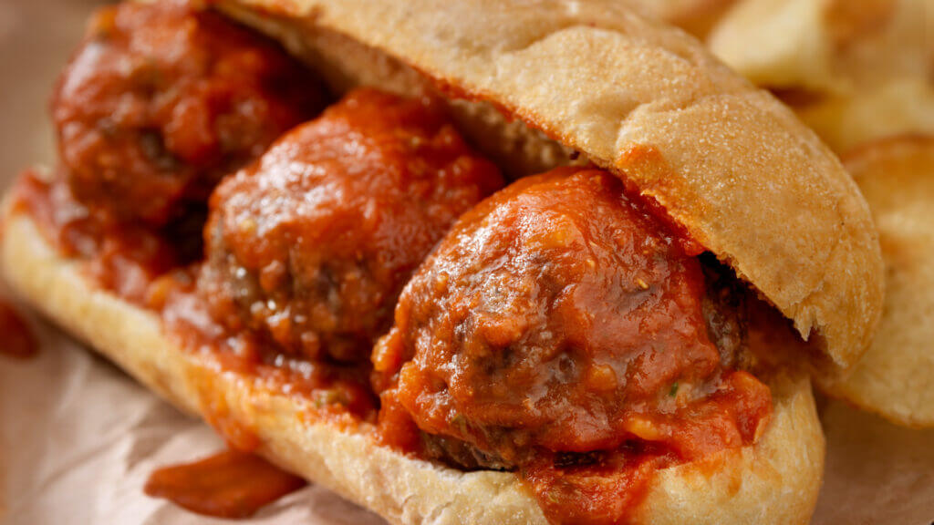 A close up of an oozing meatball sandwich. 