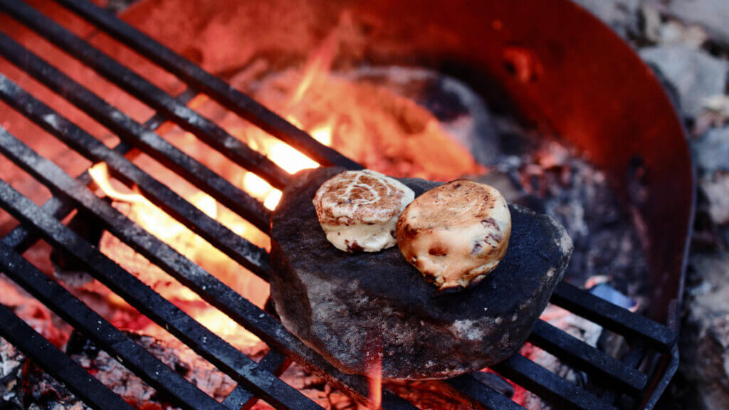 Two cinnamon rolls heat up on a rock over a campfire for an easy camping meal.