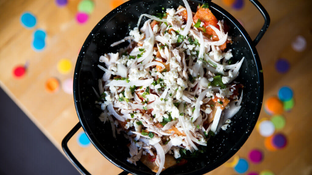 A pan full of freshly made chilaquiles above a wooden table with confetti.