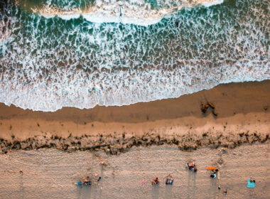 An overhead view of waves crashing on the shore with people sitting on the beach in San Diego which is a great place to beach camp in southern california.