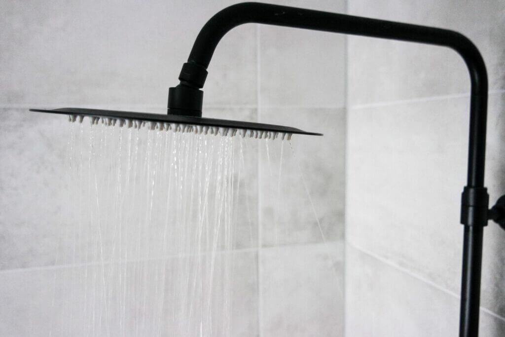 A black showerhead with running water. When you have an RV tankless water heater, you don't have to worry about running out of hot water when taking your shower. 