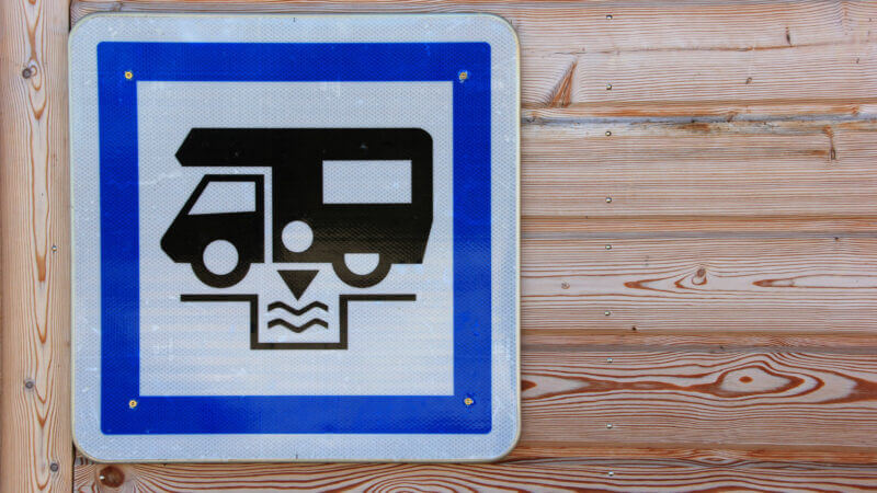 Blue and white RV dump station sign on light wood grain wall to dump dirty grey water safely.