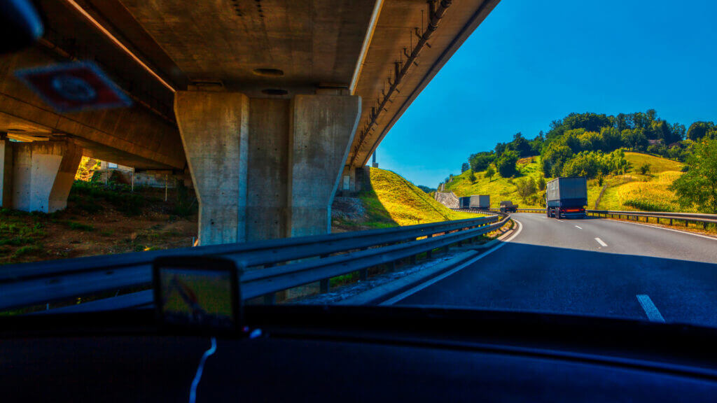 A dashboard view of an RV driving under a bridge following trucks on a highway. 