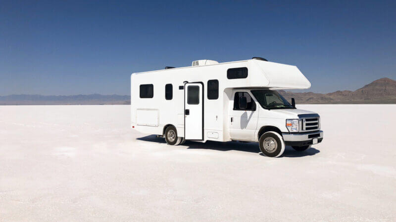 A white self-contained RV is parked in the middle of nowhere white desert, but they don't have to worry! They have everything they need onboard so they don't have to rely on campsite hookups to use the bathroom or shower.