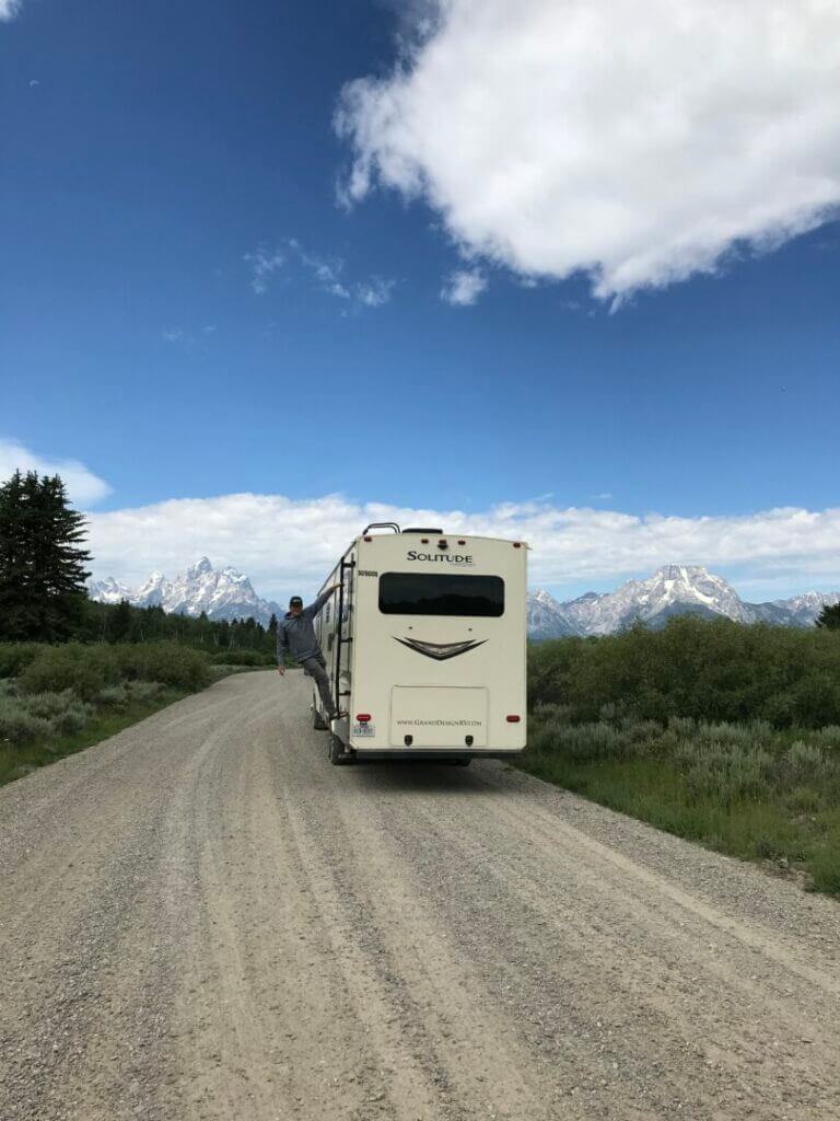 Man hanging off an RV ladder with Grand Teton National Park in the background. 