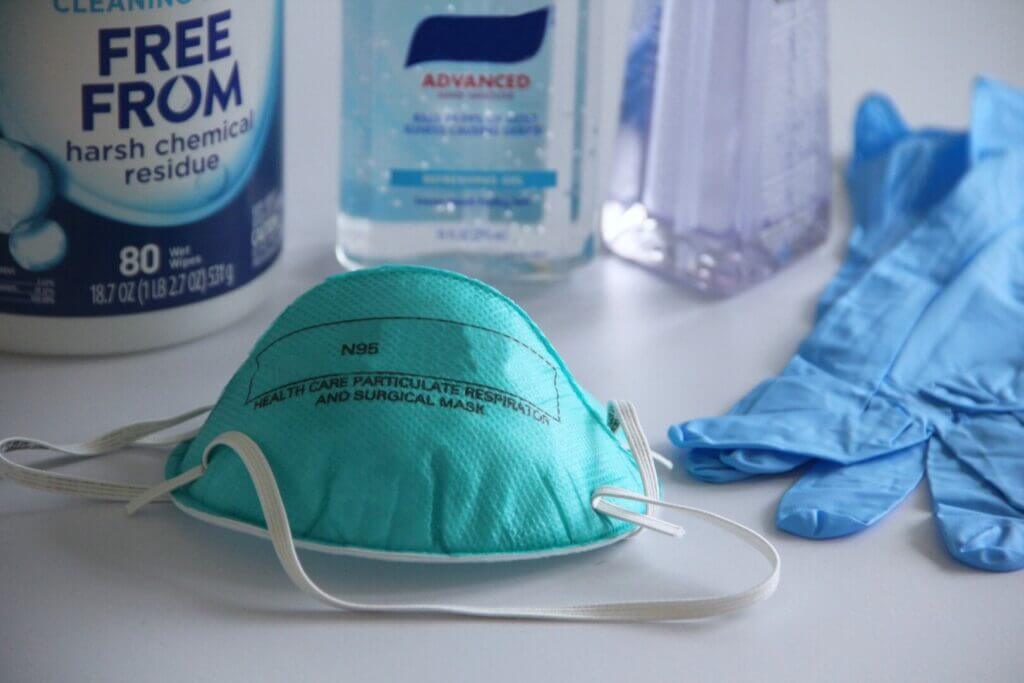 N95 mask laying on a white table with hand sanitizer and gloves around it