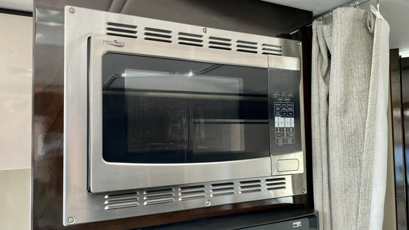 a stainless steel RV microwave mounted above the stove in a travel trailer