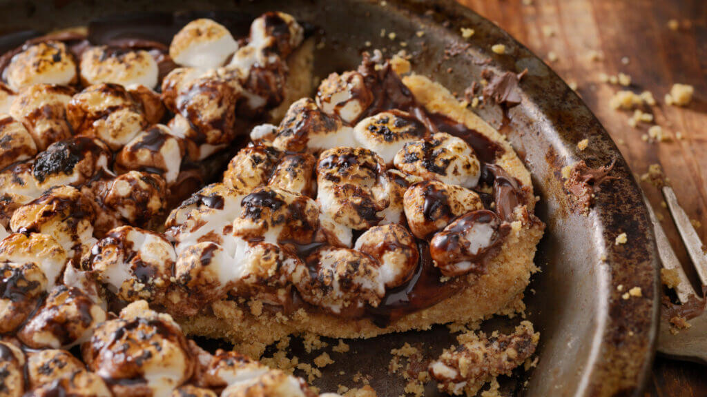A smores pizza in a pizza dish with graham cracker crumbs all over. This is one of the best smores recipes. 