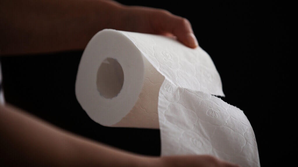 A hand pulls one sheet of toilet paper off the roll.