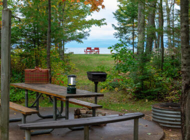 A campsite tucked into the trees looks out onto Lake Michigan with two camping chairs already set out on the shore. These are the 12 best camping spots along Lake Michigan!
