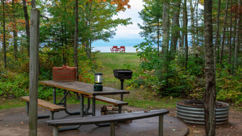 A campsite tucked into the trees looks out onto Lake Michigan with two camping chairs already set out on the shore. These are the 12 best camping spots along Lake Michigan!