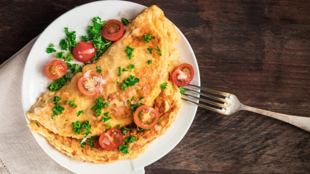 A breakfast omelet with tomatoes garnished on top and a fork beside the plate ready to eat!