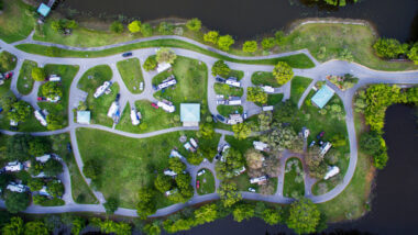 An aerial view of an RV park surrounded b y water and greenery which would be an ideal location to live in your RV full time.