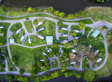 An aerial view of an RV park surrounded b y water and greenery which would be an ideal location to live in your RV full time.