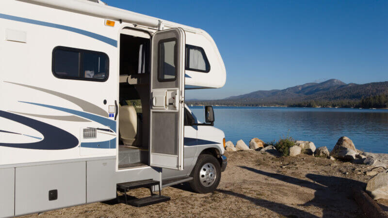 A white rv parked near water has the door open and some steps that can be upgraded to one of these listed best RV steps!