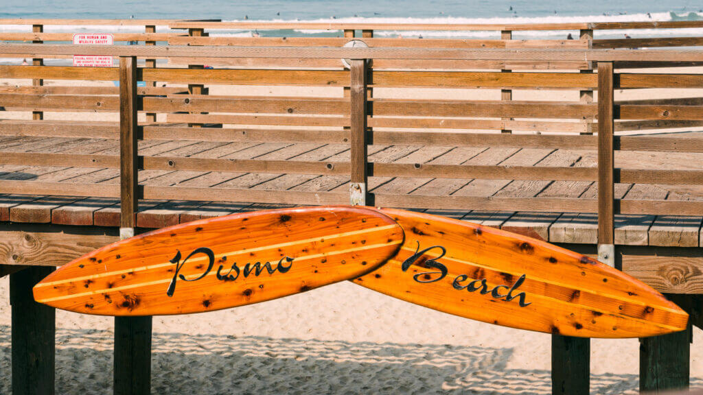 Pismo Beach pier is decorated with two wooden surfboard signs. Pismo Beach is a great place to visit and camp!