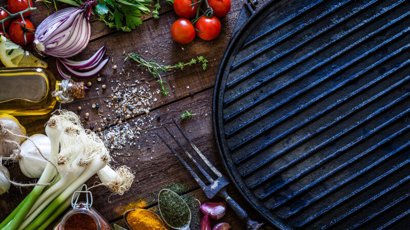 A blackstone griddle is surrounded by spices and veggies and ready to cook some delicious lunch recipes.