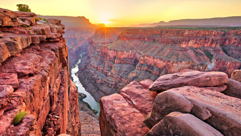 The grand canyon glows red orange with the sun setting on the horizon and the river glows below. A great place to visit in your RV.