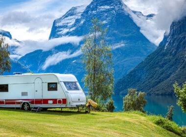 An RV is parked on a grassy hill next to a stunning glacier lake set in the mountains. By using a levelmate pro they can ensure that their RV is level and secure.