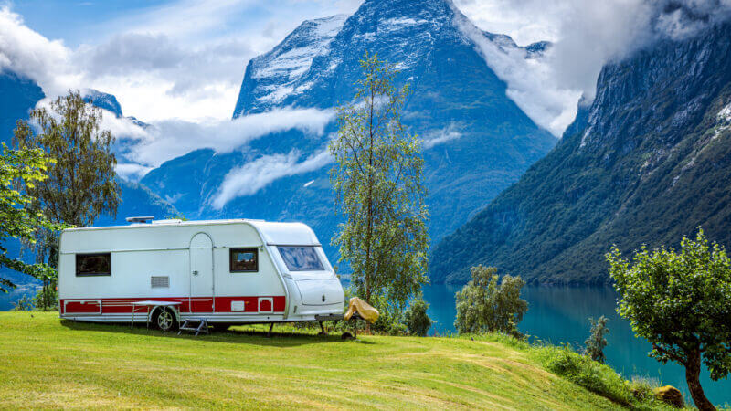 An RV is parked on a grassy hill next to a stunning glacier lake set in the mountains. By using a levelmate pro they can ensure that their RV is level and secure.