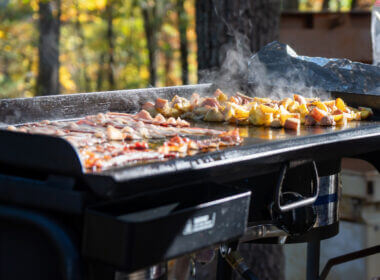 A blackstone griddle is topped with breakfast classics and makes the best meals! This one is being used at an RV campsite outside in the woods.