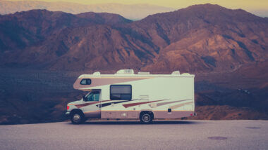 An rv parked in a open lot with hills in the background. Anyone can RV on a budget with these money saving tips!
