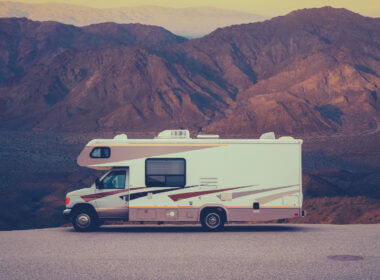 An rv parked in a open lot with hills in the background. Anyone can RV on a budget with these money saving tips!