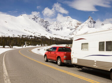 A red truck tows a travel trailer along a highway surrounded by snow and headed towards the snowy mountains! What is the best truck to tow a travel trailer?