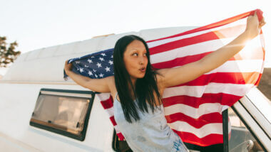 A woman holds an American flag outside the window of her RV as she sets out on her RV trip across all 50 states.