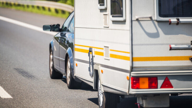 A small SUV tows a travel trailer rental with yellow stripes down the highway.